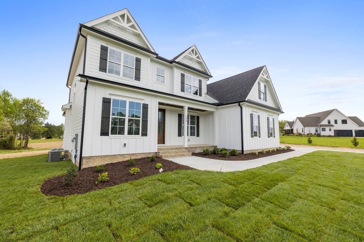 White two-story American middle class suburban home with green lawn and blue sky